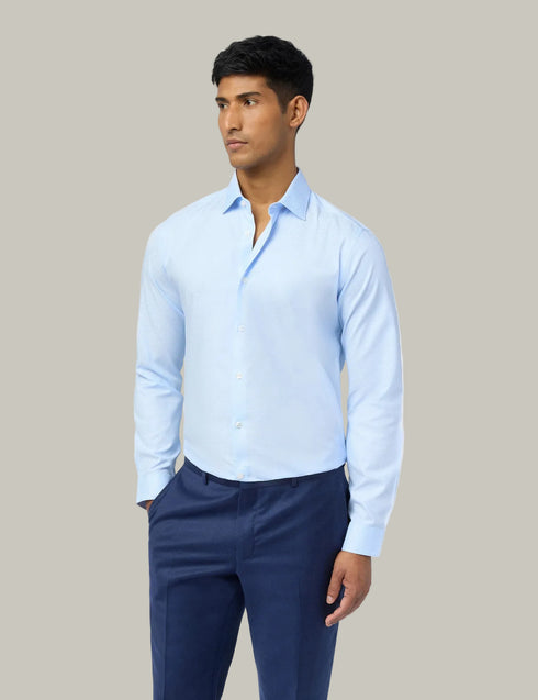 Man wearing a light blue shirt and navy pants against a plain background