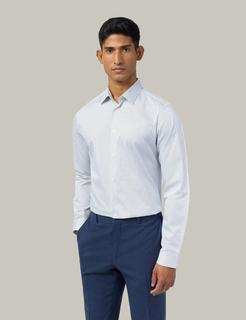 Man wearing a light blue patterned shirt and navy pants on a white background