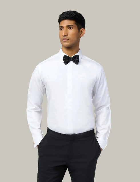 Man wearing a white dress shirt with a black bow tie and black pants on a light gray background