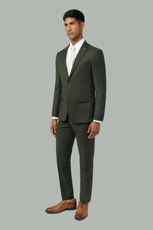 Man wearing a green suit with a white shirt and brown shoes on a light gray background