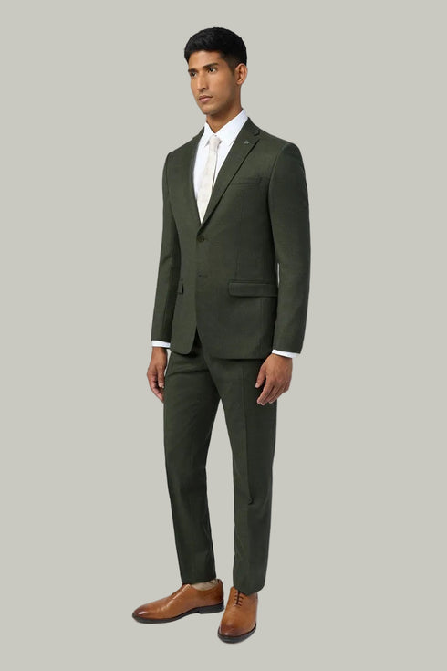 Man wearing a green suit with a white shirt and brown shoes on a light gray background